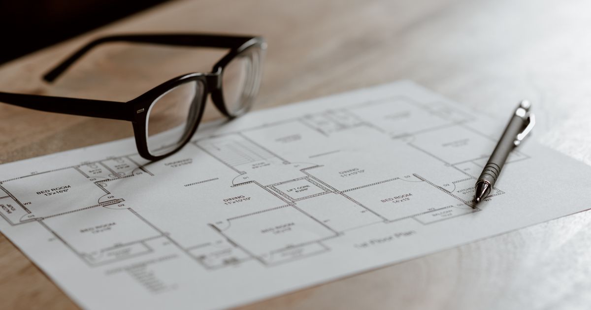From above of eyeglasses near pen on plan placed on wooden table in apartment in soft daylight