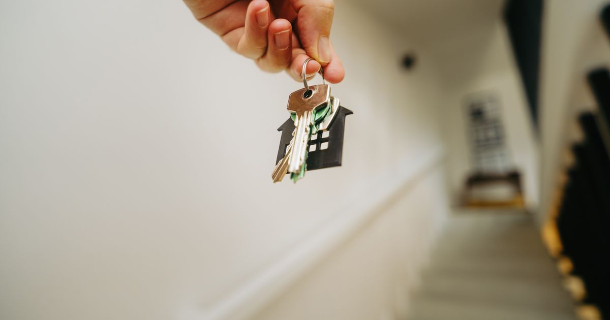 Close-up of a hand holding a keychain in the shape of a house, symbolizing real estate and property ownership.
