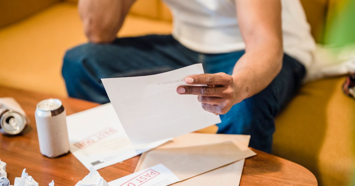 Man sitting on sofa reading unpaid bills, looking stressed and concerned over financial debt.