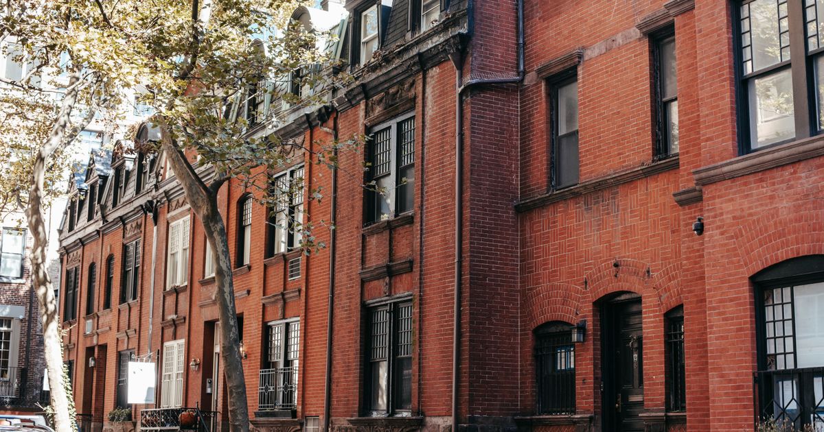 Exterior of aged brick residential building with windows and stairs located on city street on sunny autumn day